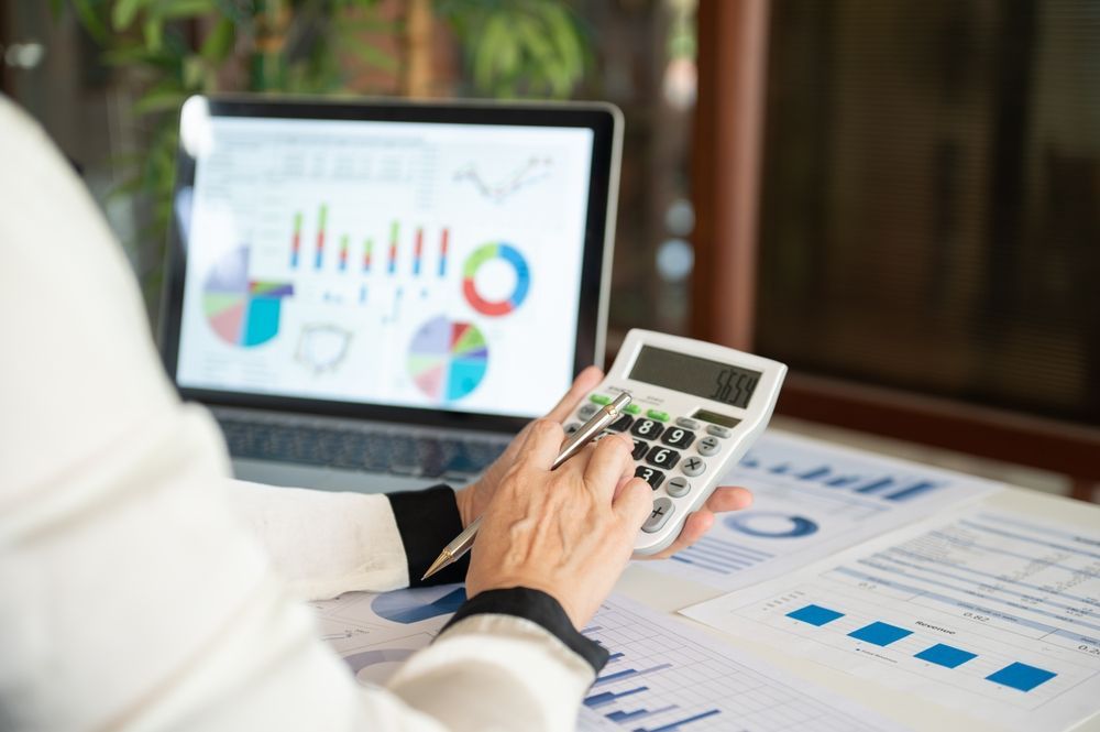 Person using a calculator, looking at charts on a laptop and printed documents.