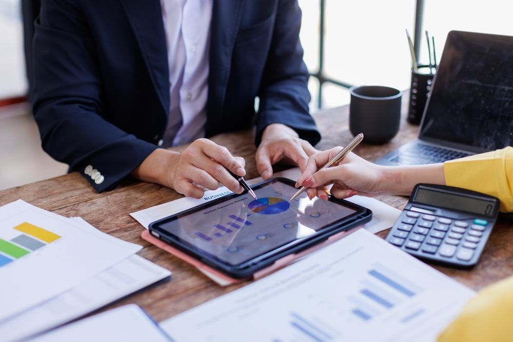 People reviewing financial data on a tablet. Documents, calculator, and laptop on the table.