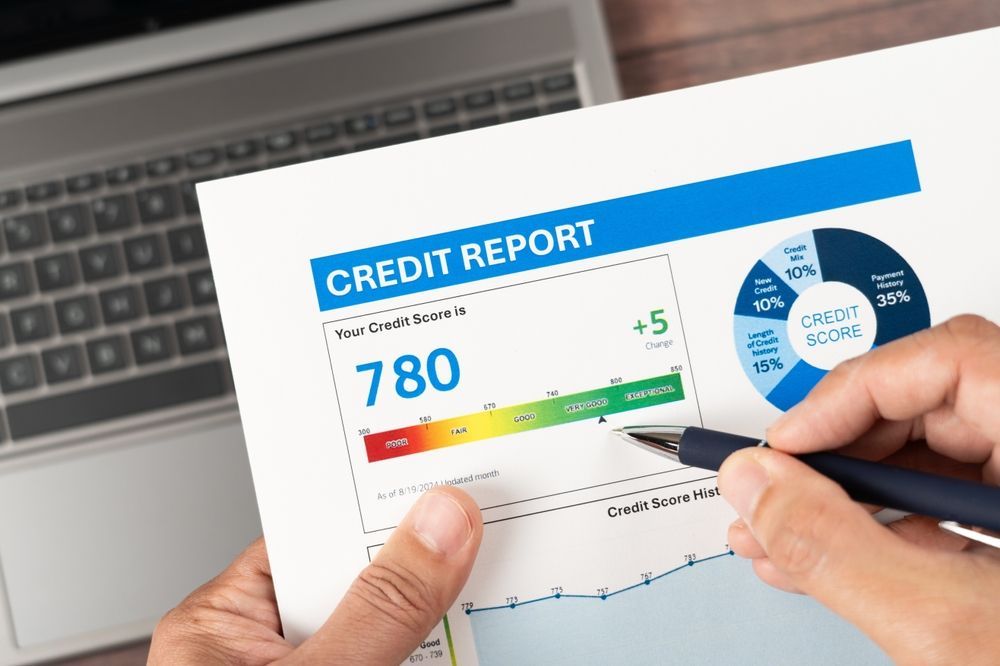 Person holding a credit report; score of 780 highlighted with a pen, next to a laptop.