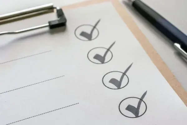 Checklist with several check marks on a clipboard beside a pen
