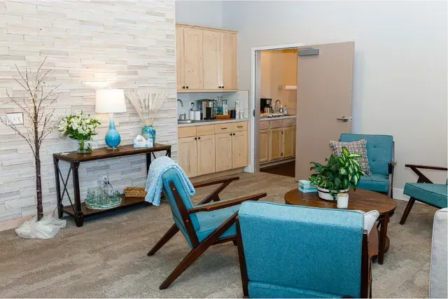 Modern living room with turquoise chairs, wooden table, side console, and open doorway to a kitchen.