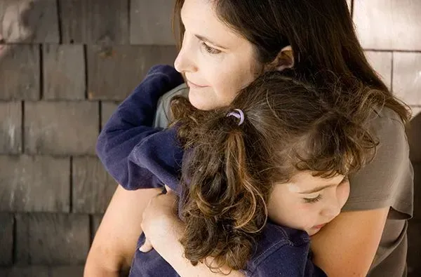 Woman hugging a sleeping child on a wooden bench, both in dark blue clothing