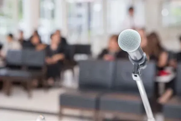 Microphone on stand in a blurred conference room with people seated in the background