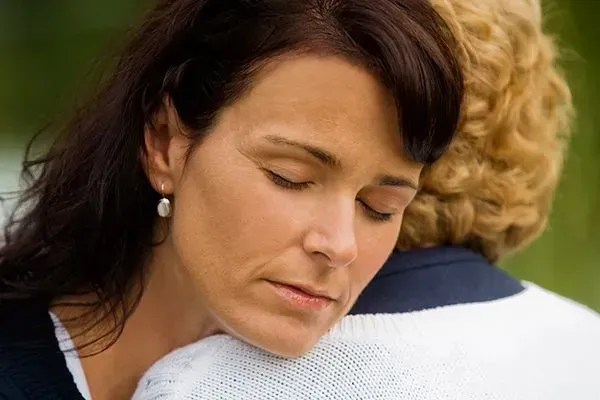Two people embracing outdoors, one with eyes closed and a calm expression