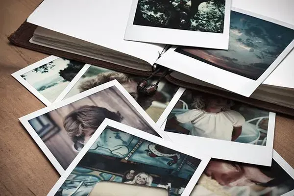 Scattered printed photos and a brown leather strap on a wooden table