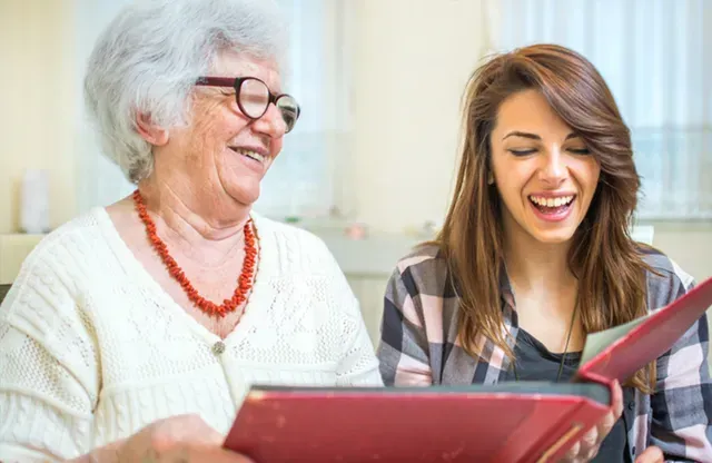 Two women smiling while reading a red book together indoors