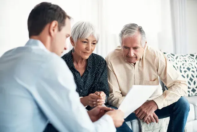 Three people reviewing documents together on a couch in a bright living room