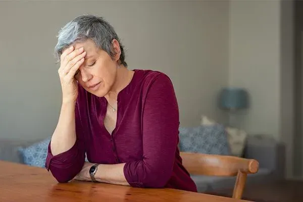 Woman in maroon top resting her head in her hand at a table, looking stressed or tired