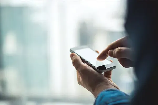 Person using a smartphone with one hand and tapping the screen with the other in a bright indoor setting