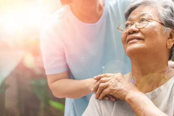 Person gently holding hands with an elderly woman outdoors in warm sunlight