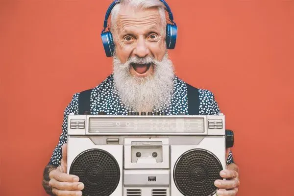 Smiling elderly man in blue headphones holding a boombox against a coral background