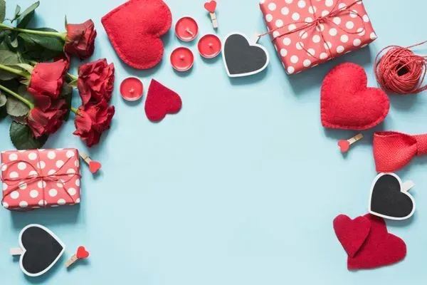 Valentine-themed flat lay with red roses, heart decorations, and wrapped gift boxes on a light blue background