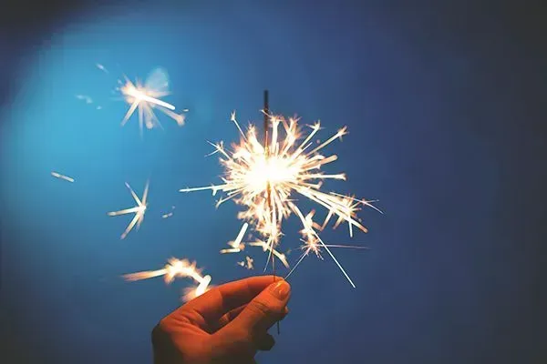 Hand holding a lit sparkler against a dark blue background