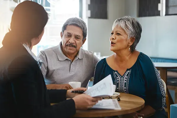 Three people talking at a table, with papers and coffee in a bright office.