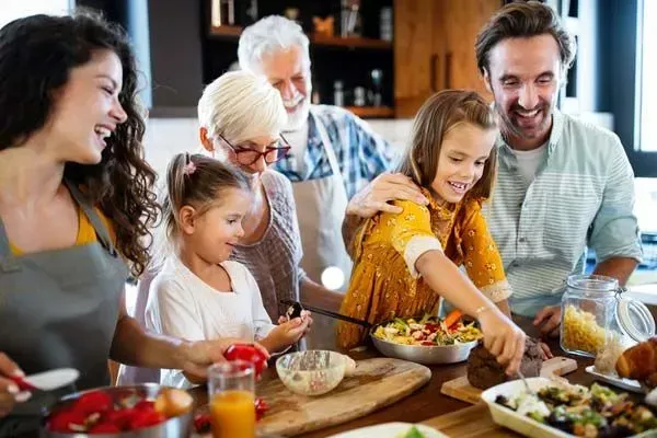 Family sharing a meal together at a dining table, smiling and serving food in a warm kitchen.