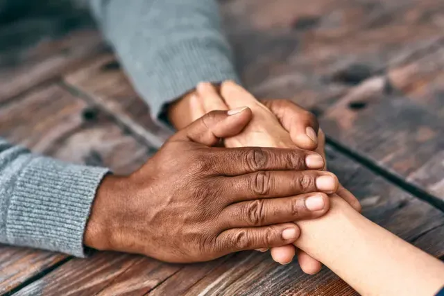 Two hands stacked in a gesture of support on a wooden table