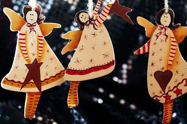 Three handmade angel ornaments with star and heart accents, hanging against a dark blurred background