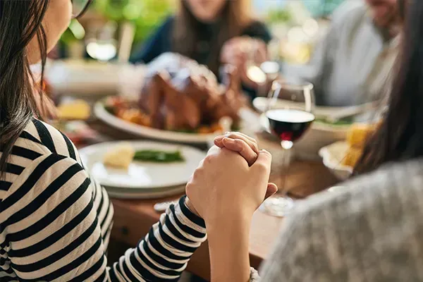 Two people holding hands at a dinner table with a roast turkey and wine glasses in the background
