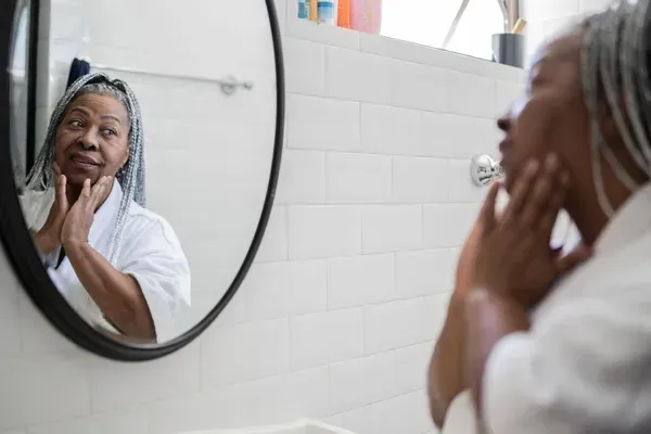 Person looking at their reflection in a bathroom mirror while touching their face