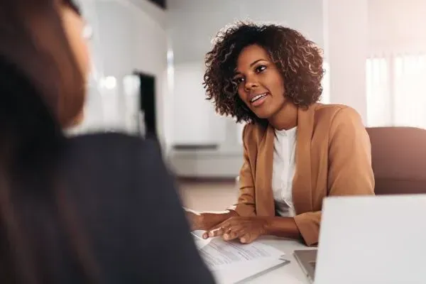 Two people in a bright office discussing documents at a desk with a laptop