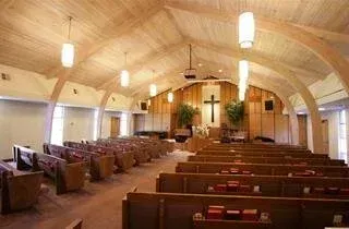 Empty church sanctuary with wooden pews, arched ceiling, hanging lights, and a cross at the altar