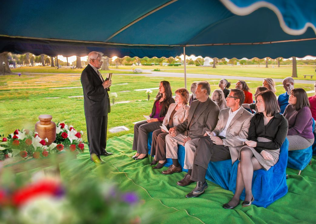 Speaker addressing seated audience under a tent on a grassy lawn at dusk