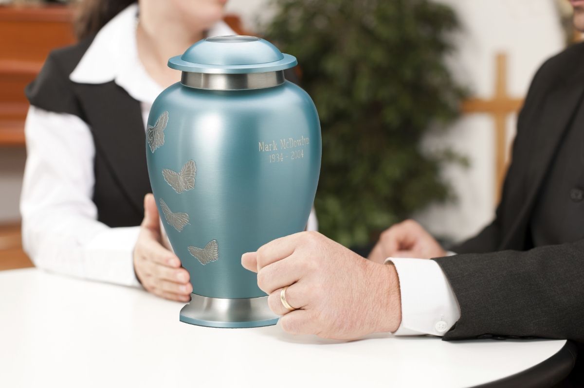 Two people holding a blue urn on a white table in a formal setting