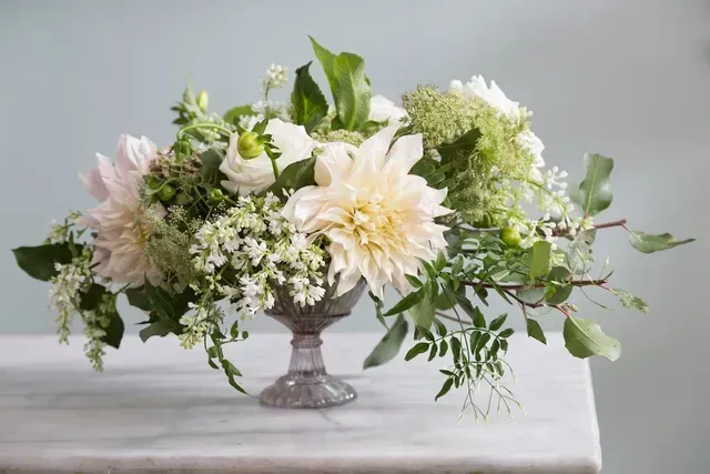 White and pastel flower arrangement in a silver vase on a table