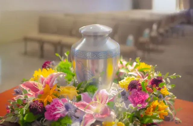 Silver urn surrounded by colorful flowers on a table in a softly blurred room