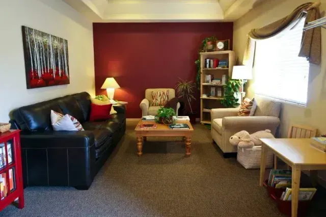 Cozy living room with black and cream sofas, red accent wall, coffee table, and bright window with drapes