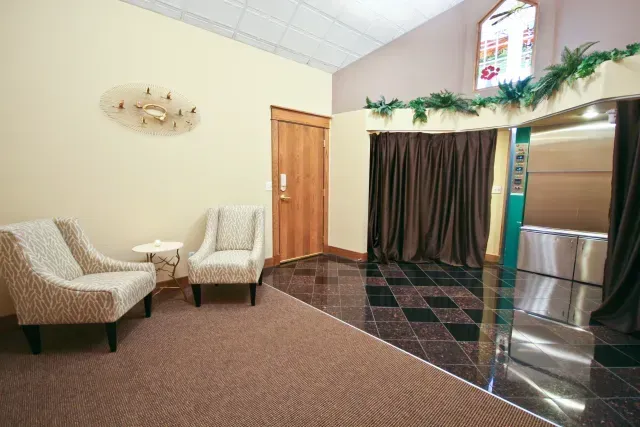 Quiet lobby with two cream chairs, small table, wooden door, and curtain-covered doorway with greenery above.