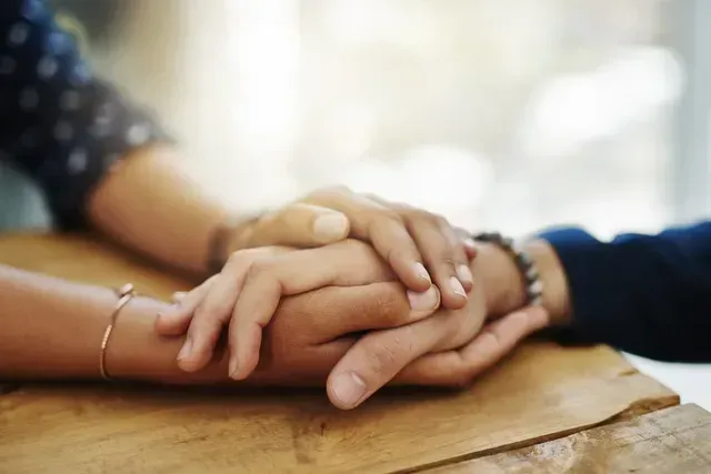 Hands stacked together in a supportive gesture on a wooden table
