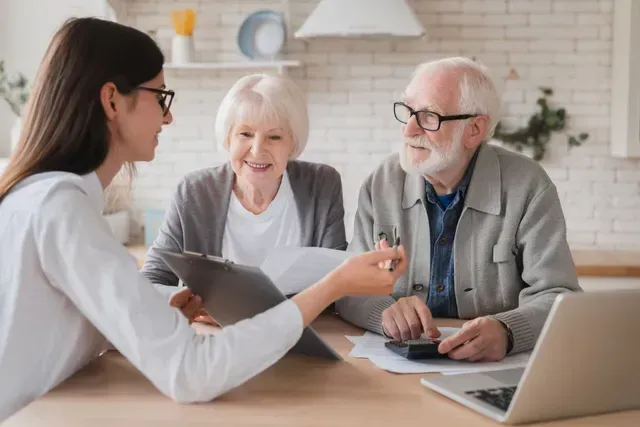 Health consultant meeting with two clients at a table, reviewing documents on a laptop in a bright office.