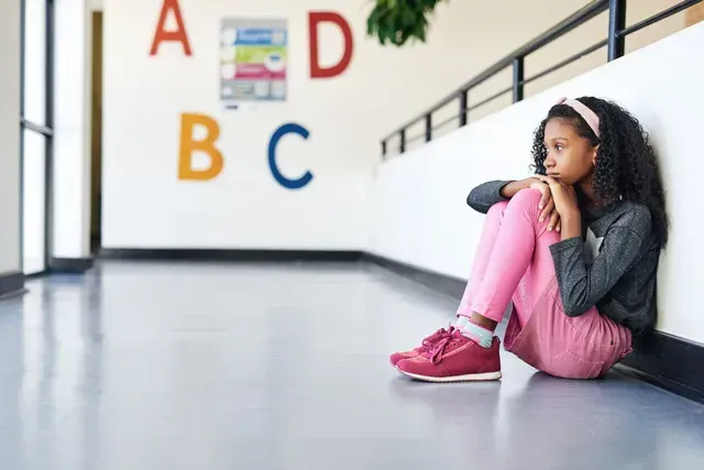 Child sitting on a school hallway floor beside colorful alphabet letters on the wall