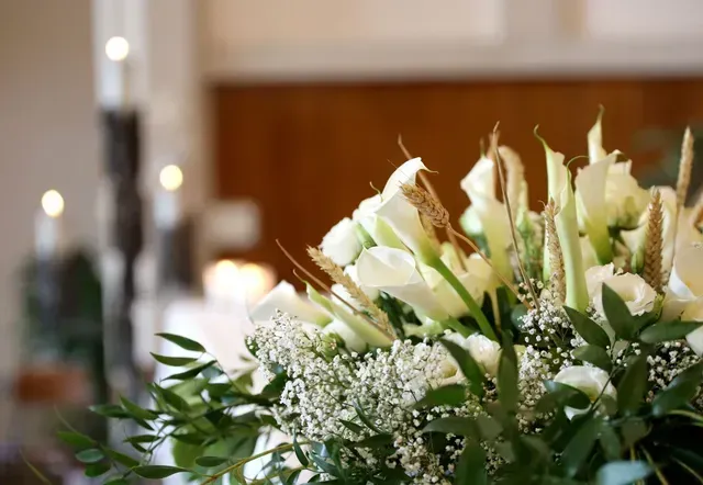White lilies and greenery arranged on a table in a softly lit indoor setting