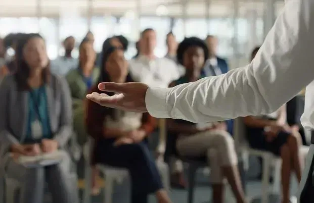 Speaker gesturing toward seated audience in a bright meeting room