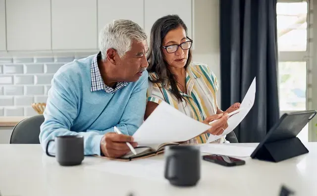 Two coworkers reviewing documents at a table, with a laptop and coffee mugs nearby.
