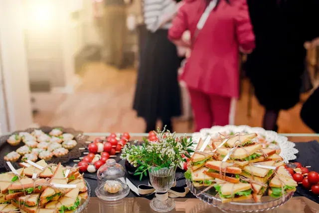 Dessert table with cupcakes, berries, and stacked sandwiches at a blurred indoor party or reception
