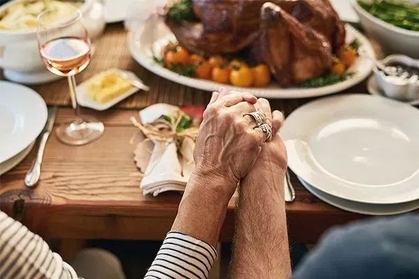 Hands clasped at a dinner table beside plates and a roasted turkey centerpiece