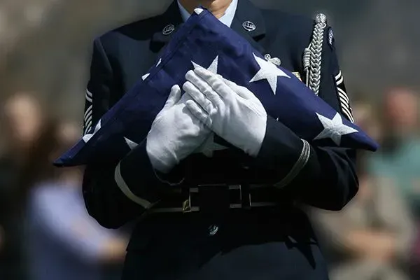 Honor guard holding a folded U.S. flag in white gloves during a military ceremony