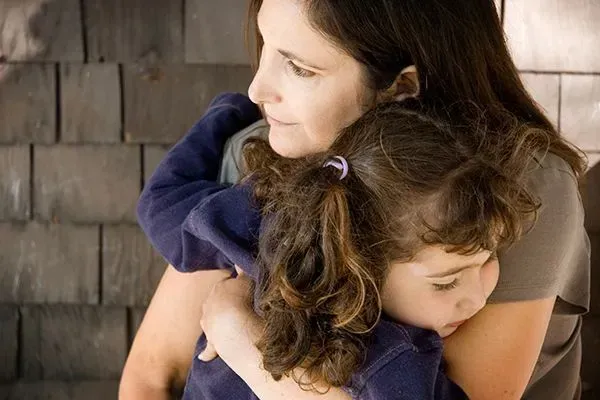 Woman hugging a small child indoors against a wooden wall