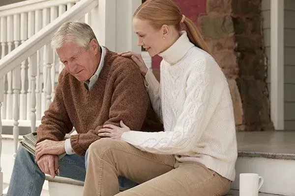 Two people sitting on front steps, one comforting the other outdoors
