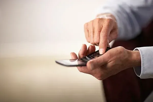 Hands tapping a smartphone on a couch, with a blurred light background.