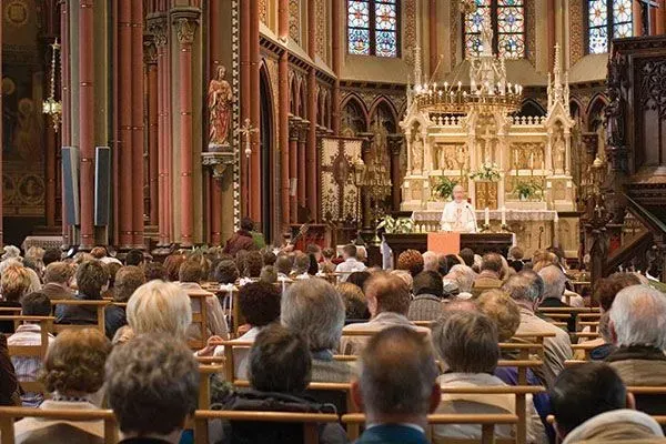 People seated in a grand cathedral during a ceremony, facing a lit altar.