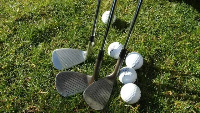 Golf clubs and four white golf balls on green grass