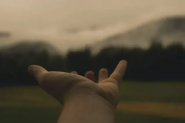 Outstretched hand reaching toward a cloudy sunset over a dark field
