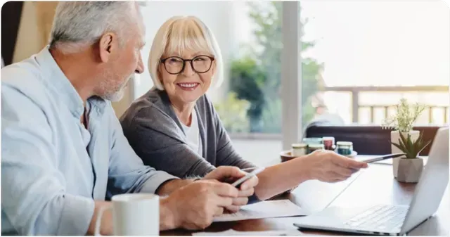 Two people discussing paperwork at a bright office table, with a laptop and coffee cups nearby.