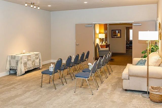 Conference room with rows of blue chairs, beige carpet, and a cream sofa by a doorway.