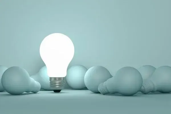 Glowing lightbulb among matte blue bulbs on a soft blue background