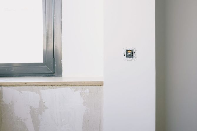 Partially painted wall beside a window with exposed plaster and a small outlet opening